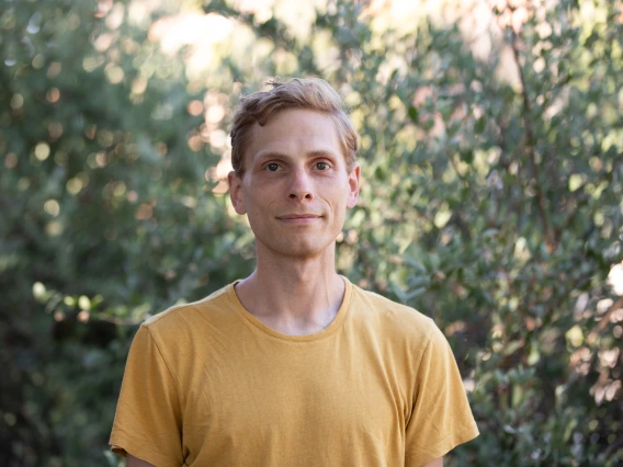 Photo of Andrew Slemmon wearing a yellow t-shirt against a background of sun-dappled leaves