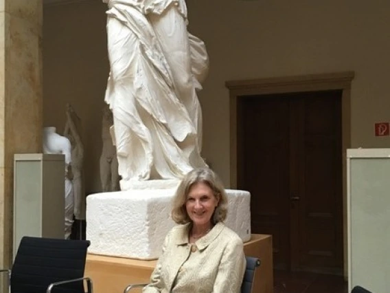 Dr. Irene Romano sits smiling in front of a piece of statuary
